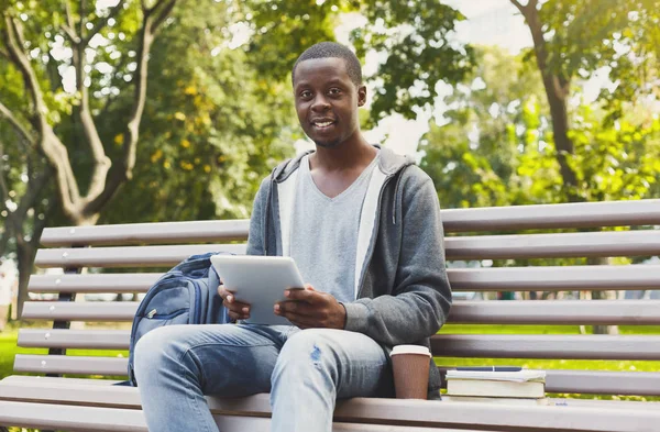 Улыбающийся африканско-американский студент в парке с табличкой на открытом воздухе — стоковое фото