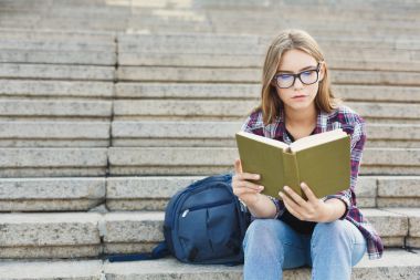 Genç kadın Üniversitesi merdivenlerde kitap okuma