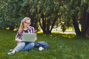 Parkta dizüstü bilgisayar kullanan mutlu genç kadın