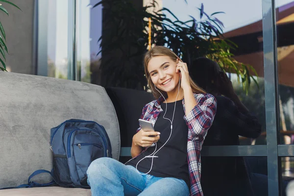 Chica joven escuchando música sentada en la cafetería — Foto de Stock