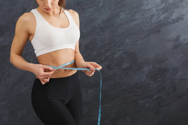 Fit woman measuring her waist closeup