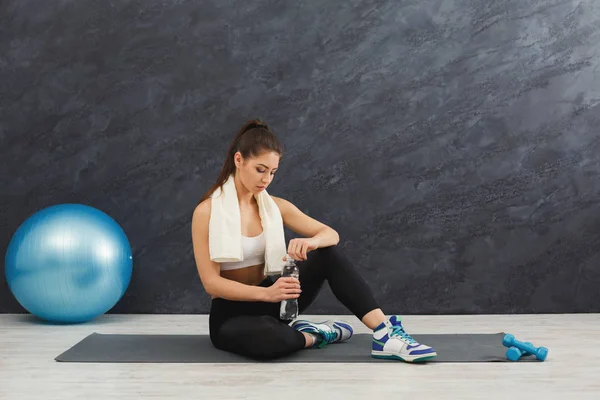 Fitness mujer beber agua en el gimnasio sobre fondo gris — Foto de Stock