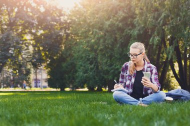 Çim üstünde defter ile oturan genç kadın