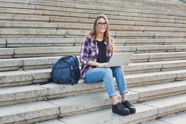 Gülümseyen öğrenci dizüstü kullanarak merdivenlerde oturan