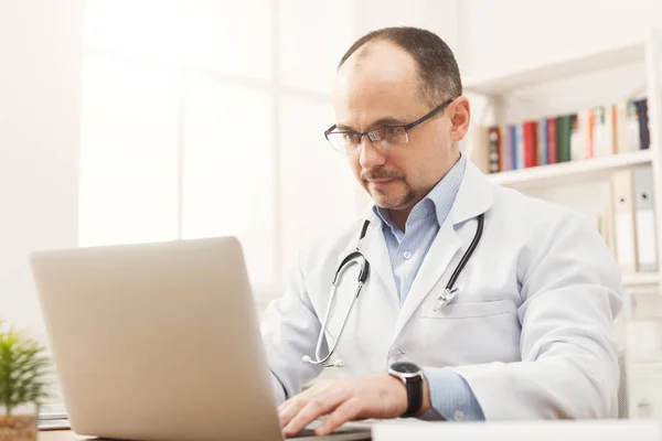 Serious doctor in glasses sitting at the desktop — Stock Photo, Image