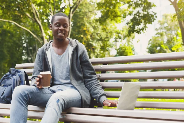 Estudiante afroamericano trabajando en un portátil y tomando café afuera —  Fotos de Stock