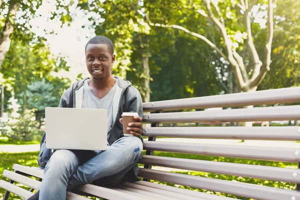 Estudante afro-americano trabalhando em um laptop e bebendo café fora — Fotografia de Stock