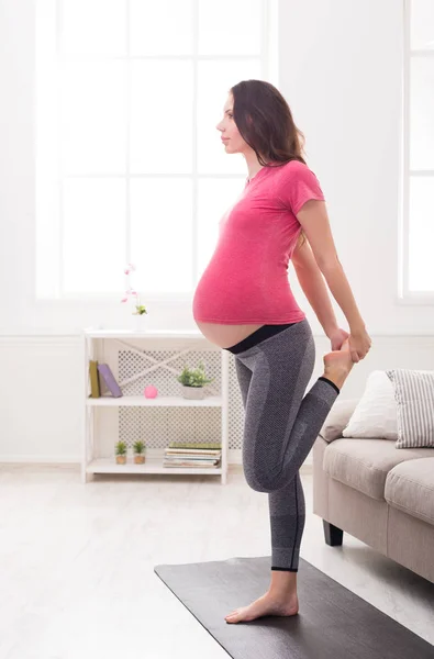 Mulher grávida alongamento pernas formação dentro de casa — Fotografia de Stock
