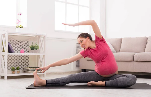 Беременная женщина, занимающаяся растяжкой в помещении — стоковое фото