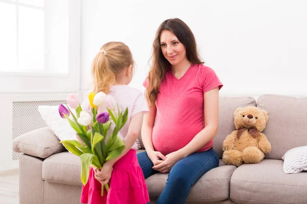 Meisje verbergen bloemen van moeder achter haar rug — Stockfoto