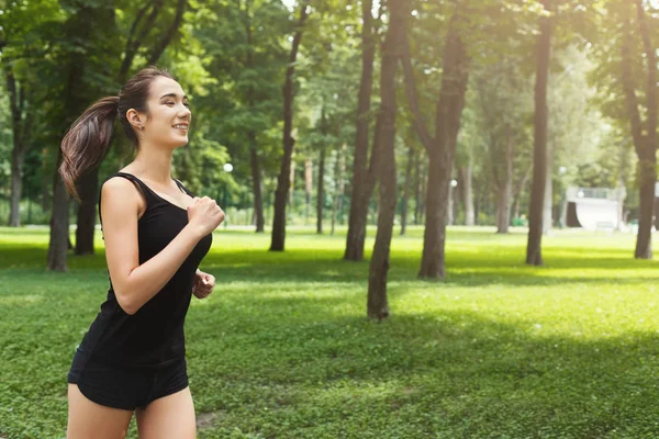 Young woman jogging in green park, copy space — Stock Photo, Image