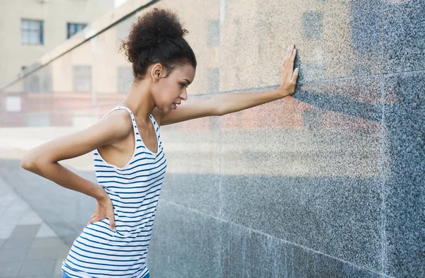 Tired woman runner is having break, leaning on grey wall