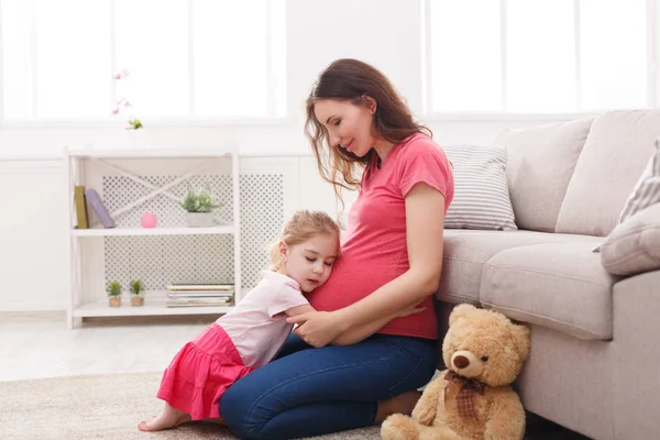 Klein meisje haar zwangere moeder buik knuffelen — Stockfoto