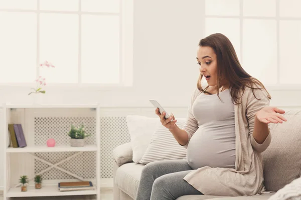 Mulher grávida surpresa usando smartphone em casa — Fotografia de Stock