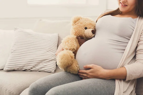 Mujer embarazada sosteniendo oso de peluche en su barriga — Foto de Stock