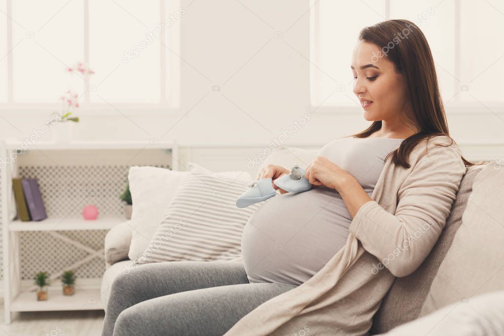 Pregnant woman holding tiny shoes near belly