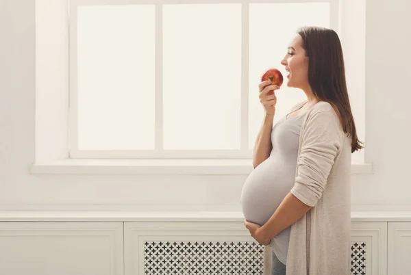 Беременная женщина ест яблоко в домашних копиях пространства — стоковое фото