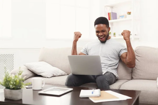 Giovane uomo nero con le braccia alzate, con il computer portatile che celebra il successo — Foto Stock