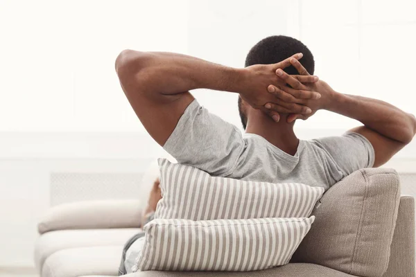 Vista trasera del hombre negro relajado en un sofá en casa a — Foto de Stock