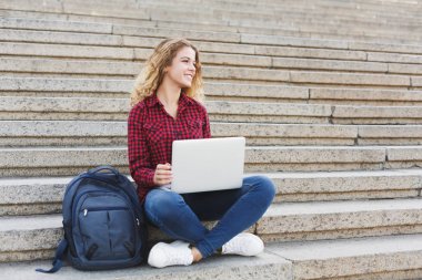 Merdivenlerde oturan ve dizüstü bilgisayar açık havada ile çalışan kız öğrenci