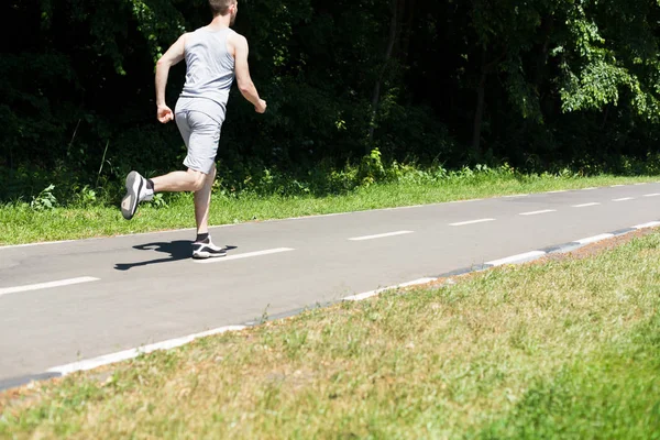 Молодой человек бегает на беговой дорожке в парке, копирует пространство — стоковое фото