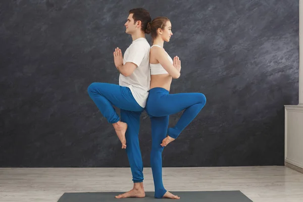 Couple training yoga in balance pose, standing back to back