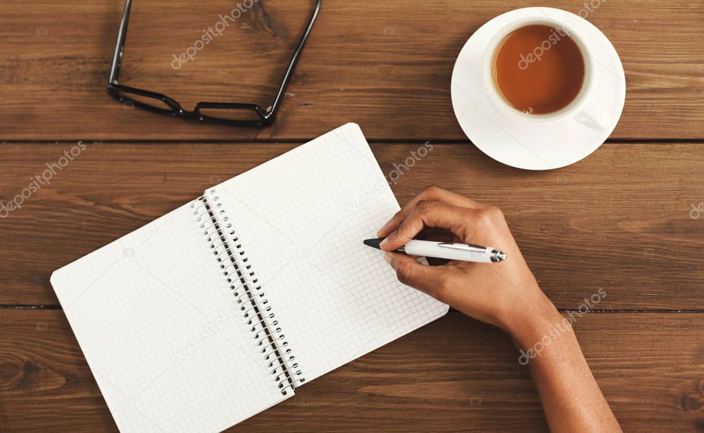Black female hands writing in notebook, top view