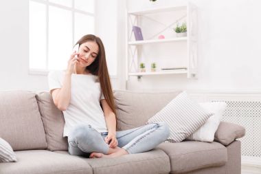 Kanepede oturan ve cep telefonuyla konuşan genç kadın