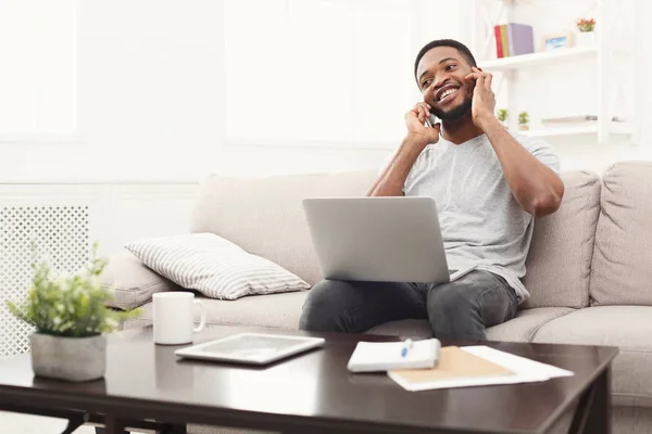 Jovem sorridente em casa com laptop e celular — Fotografia de Stock