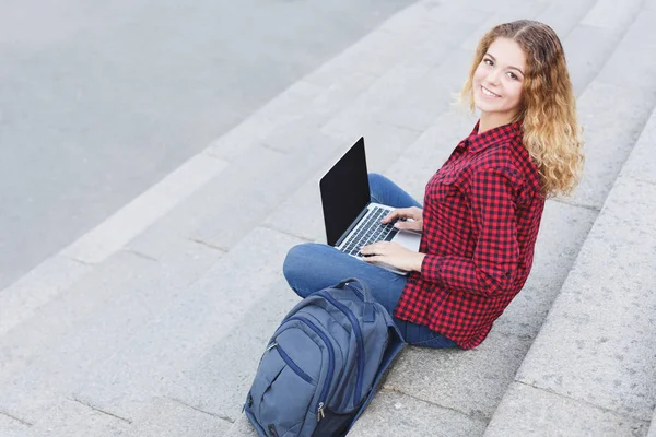 ノート パソコンを屋外で使う階段に座っている学生少女の笑みを浮かべてください。 — ストック写真