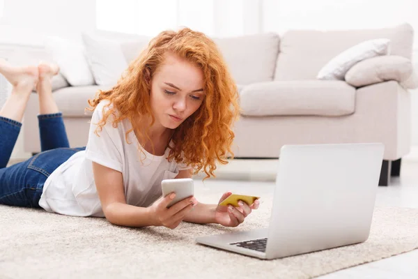 Pensive girl shopping online with laptop and phone