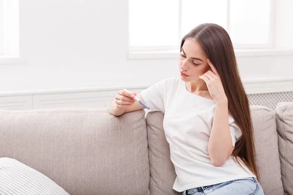 Беспокойная девушка с тестом на беременность сидит на диване — стоковое фото