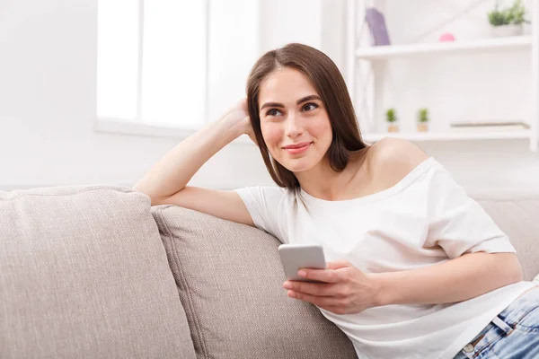 Giovane donna sorridente seduta sul divano con cellulare — Foto Stock