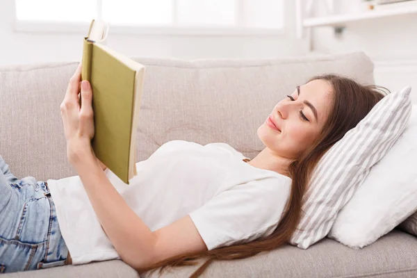 Felice giovane donna lettura libro sul divano — Foto Stock