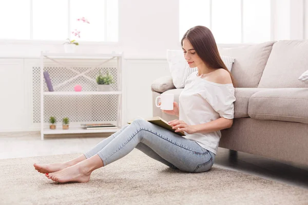 Pensive girl reading and drinking coffe on the floor — Stock Photo, Image
