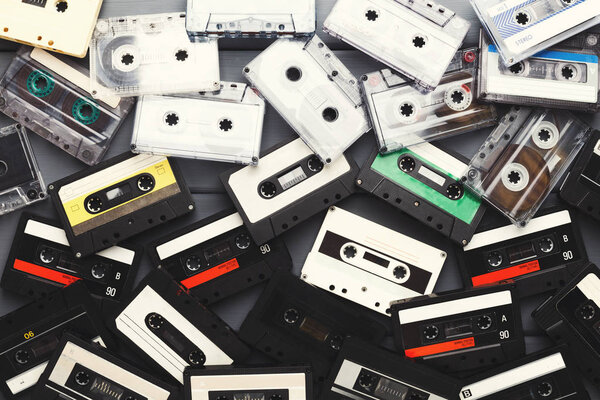 Куча винтажных аудиокассет на фоне серых досок
