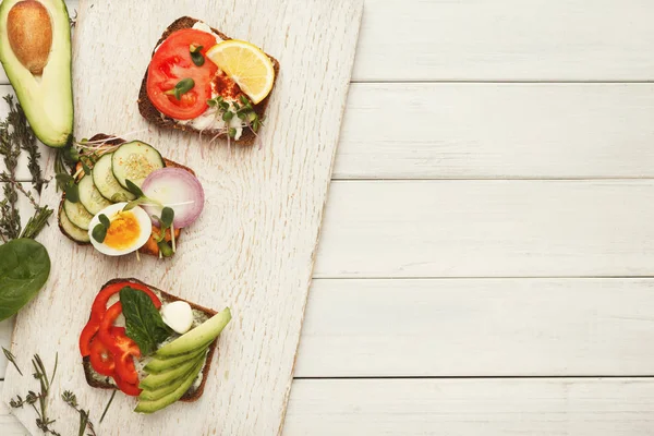 Різноманітність здорових вегетаріанських бутербродів на білому дереві, вид зверху — стокове фото