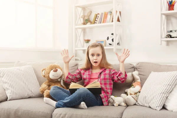 Sorprendida niña con libro y sus juguetes favoritos en casa —  Fotos de Stock