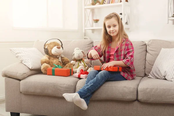 Menina bonita upwrapping presentes no sofá em casa — Fotografia de Stock