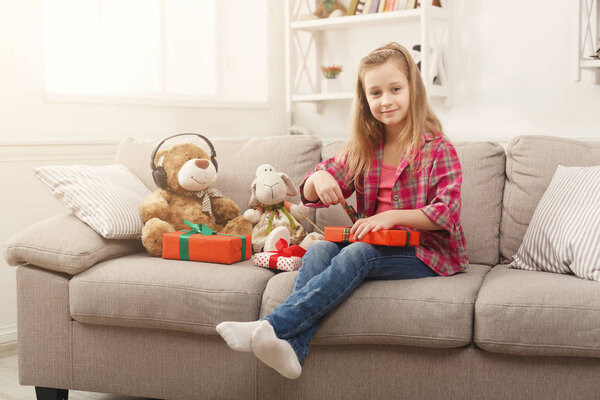Красивая маленькая девочка упаковывает подарки на диване дома
