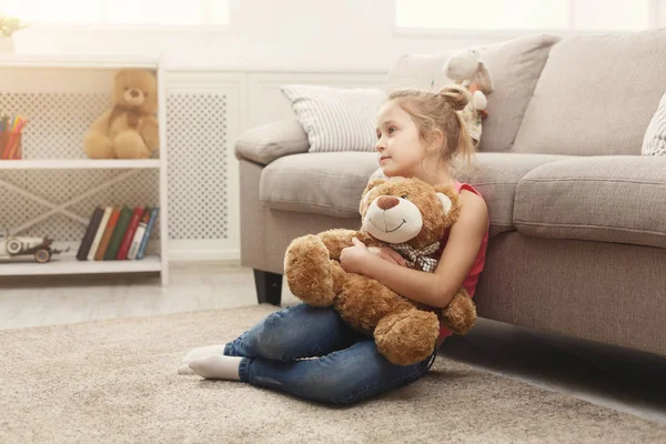 Mutlu küçük kadın çocuk oyuncak ayısının yerde evde sarılma