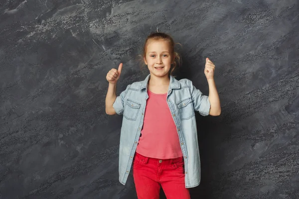 Casual niña mostrando el pulgar hacia arriba en el fondo gris — Foto de Stock