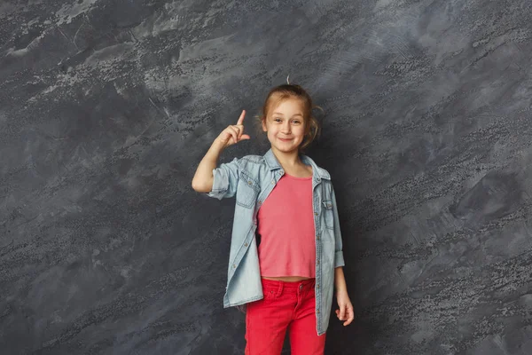 Lässiges kleines Mädchen zeigt Finger nach oben bei grauem Hintergrund — Stockfoto