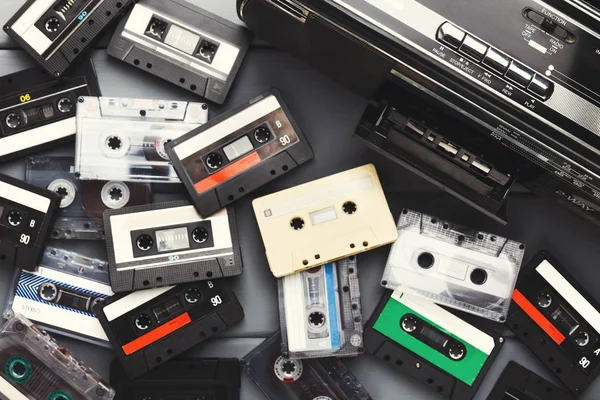 Heap of vintage audio cassettes and tape recorder at gray background