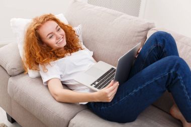 Evde boş vaktinizi. Kanepe üstünde laptop ile mutlu kız