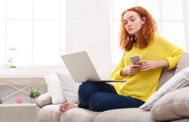 Laptop ve cep bej kanepe kullanan kız