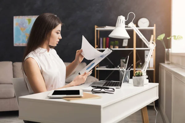 Mujer seria en casa trabajando en el ordenador portátil y la lectura de documentos — Foto de Stock