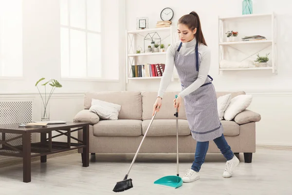 用扫帚和勺子清扫房子的年轻妇女 — 图库照片