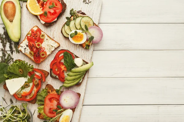 Разнообразие здоровых вегетарианских бутербродов на белом дереве, вид сверху — стоковое фото