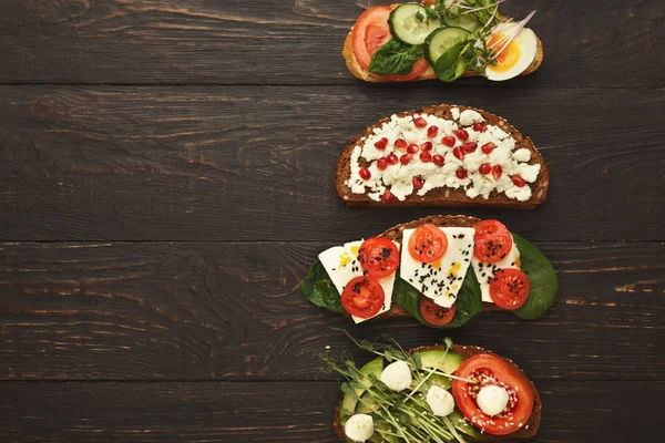 Variety of healthy vegetarian sandwiches on dark wood, top view — Stock Photo, Image